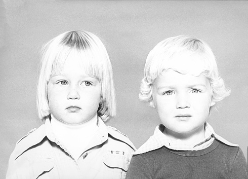 Monochrome 1978 portrait of a side-eyeing girl with blond hair and a boy with blond hair looking at the camera.