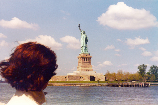 Vintage 1980s atmospheric image of woman seen from behind looking at the Statue of Liberty in New York, USA.