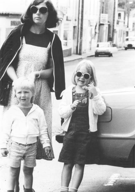 Monochrome vintage 1970s image: mother wearing sunglasses, running errands with her young daughter and son. Monochrome vintage 1970s image: mother wearing sunglasses, running errands with her young daughter and son. 1970s woman stock pictures, royalty-free photos & images
