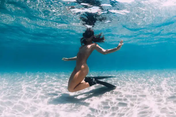 Photo of Woman free diver with fins posing over sandy sea. Freediving underwater in blue ocean