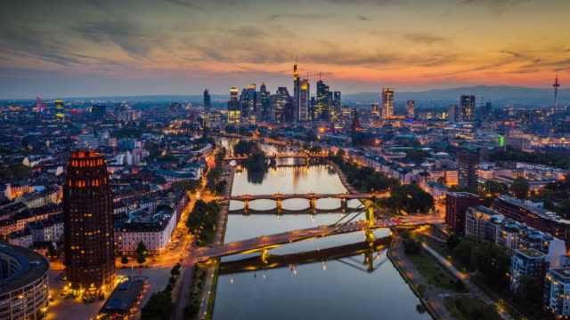 Aerial Hyperlapse shot of Frankfurt am Main skyline. Main river in the foreground and skyscrapers of the financial district in the background. Moody twilight sky at dusk. Buildings are already illuminated. Frankfurt in Hesse - Germany