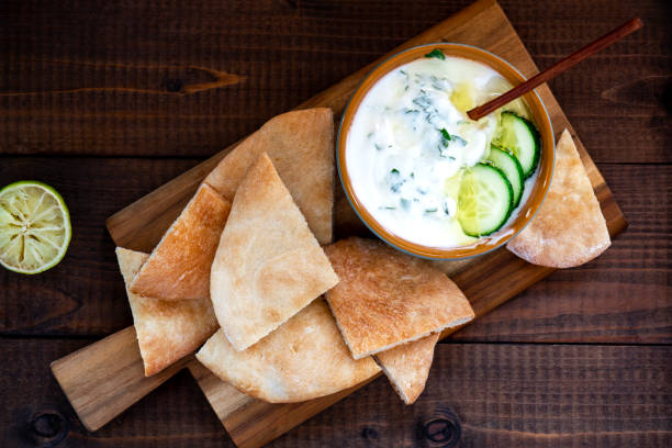 Sliced pita bread and greek yogurt Sliced pita bread and greek yogurt with cucumber, olive oil, lemon and herbs on a wooden board. Mediterranean cuisine. tzatziki stock pictures, royalty-free photos & images