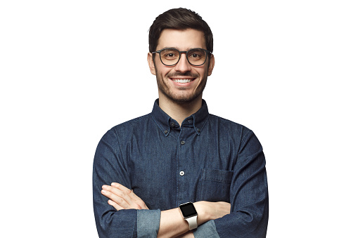 Retrato de joven hombre caucásico sonriente con los brazos cruzados, usando reloj inteligente y camisa de mezclilla casual, aislado en blanco photo