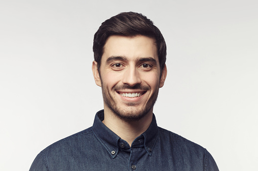 Close-up portrait of young smiling man in denim shirt isolated on gray background