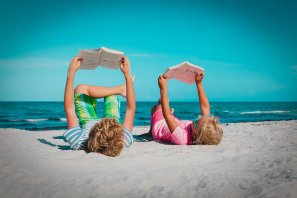 boy and girl reading books at beach vacation stock photo