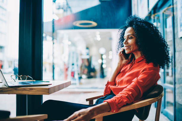 istock Cheerful dark skinned female graphic designer laughing while talking with friends on smartphone device during distance job at laptop computer.Positive african american businesswoman calling on phone 1171169849