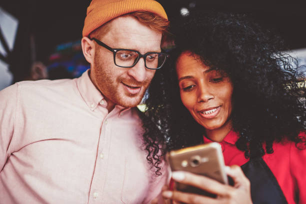 istock Multicultural two friends reading funny news on websites on modern smartphone using 4G internet connection.African american waitress showing location on mobile app of phone caucasian hipster guy 1171169932