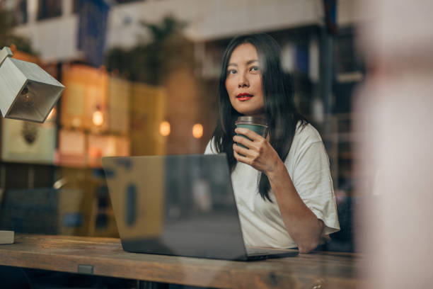 молодая женщина, работающая на ноутбуке в кафе - window reflection сто�ковые фото и изображения