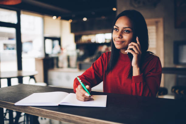 istock Attractive afro american manager noting information while talking on mobile with service operator.Dark skinned business woman having conversation on cellular about planning project writing in notebook 1171171966