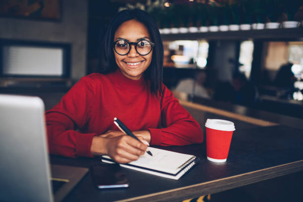 istock Cute afro american student preparing project for homework in coffee shop using free wifi access for research.Dark skinned hipster girl in eyeglasses making notes doing creative task in cafe 1171172032