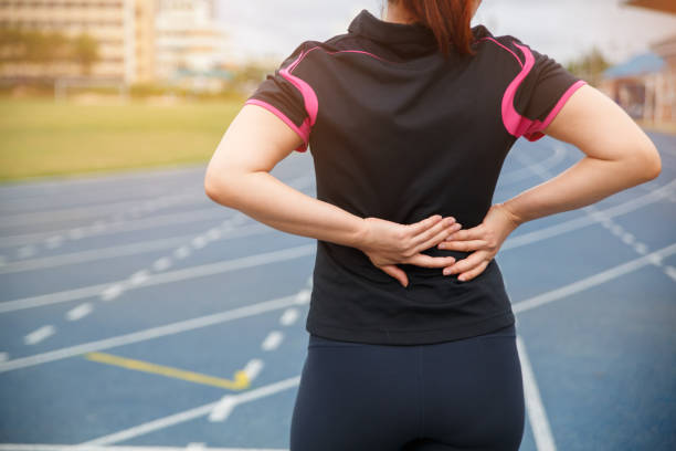 Female runner athlete back injury and pain. Woman suffering from painful lumbago while running on the blue rubberized running track. Female runner athlete back injury and pain. Woman suffering from painful lumbago while running on the blue rubberized running track. rubberized stock pictures, royalty-free photos & images