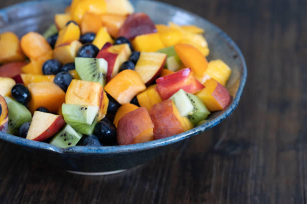 Colorful fresh fruit salad in dark bowl on wooden table in daytime stock photo