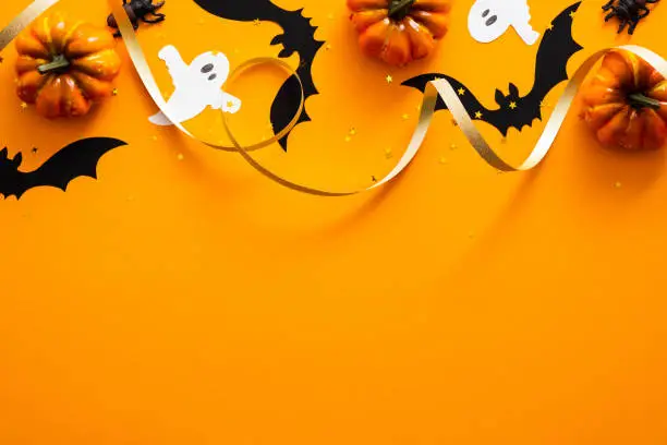 Photo of Happy halloween holiday concept. Halloween decorations, pumpkins, bats, ghosts on orange background. Halloween party greeting card mockup with copy space. Flat lay, top view, overhead.