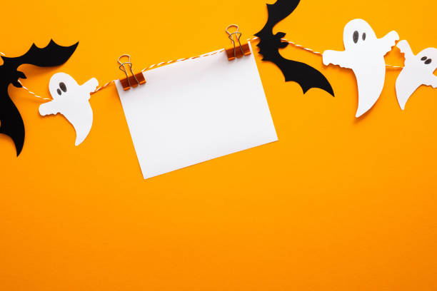 Happy halloween concept. Halloween decorations, blank paper card on clips, bats, ghosts on orange background. Halloween party greeting card mockup with copy space. Flat lay, top view, overhead. feliz concepto de halloween. decoraciones de halloween, tarjeta de papel en blanco en clips, murciélagos, fantasmas sobre fondo naranja. maqueta de tarjeta de felicitación de fiesta de halloween con espacio de copia. plano, vista superior, arriba.