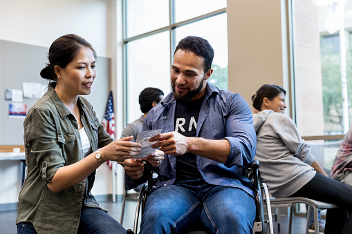 A mid adult woman shares an informational handout for veterans with an army vet in a wheelchair.