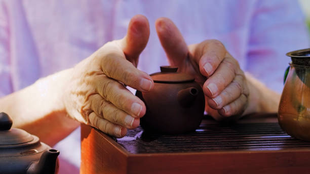 istock older man’s hands wrap around clay teapot, steeping tea, serene 1171204771