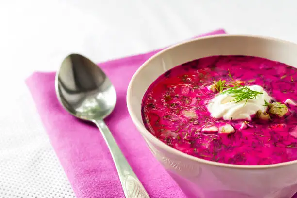 Holodnik - traditional Lithuanian (Russian, Ukrainian, Belorussian, Polish) cold beetroot soup with cucumber, boiled eggs and greens in white bowl on purple cloth