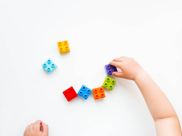 l'enfant joue avec les blocs colorés de constructeur. mains d'enfant avec le jouet de briques sur le fond blanc. jouet éducatif, plat laïc, vue du haut. - bébé cubes photos et images de collection