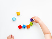 Child is playing with colorful constructor blocks. Kid's hands with bricks toy on white background. Educational toy, flat lay, top view.