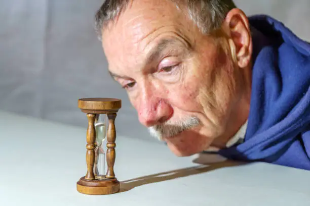 Senior man watching a time slip away as sand falls through an hourglass