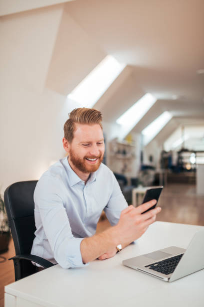 istock Happy bearded businessman using phone while sitting in office. 1171209814