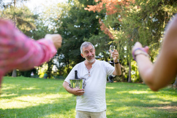 A cheerful grey haired guys offering some fresh bubbles of champagne to his two lady friends