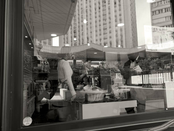 Paris, France - APRIL 23, 2019: Window of a coffee shop with a woman at the counter serving a customer and city reflection in the glass. Black and white shot