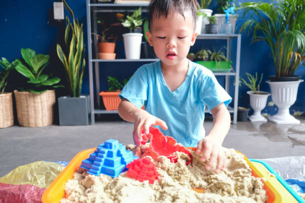 asian 3 - 4 years old toddler boy playing with kinetic sand in sandbox at home, fine motor skills development, montessori education concept - sandbox child human hand sand imagens e fotografias de stock