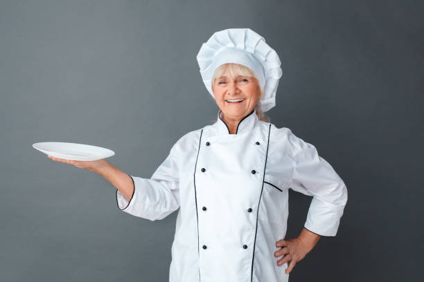 istock Senior woman chef studio standing isolated on gray holding plate looking camera laughing cheerful 1171217969