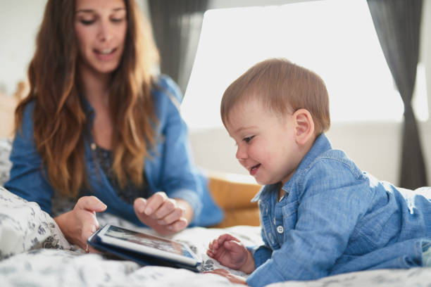 young attractive mother with female toddler child teaching to read on tablet in cosy bed - digital tablet women enjoyment happiness imagens e fotografias de stock