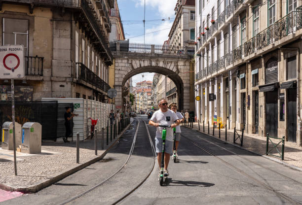 People riding a Lime electric scooter along Lisbon street Lisbon, Portugal - 9 August 2019: Man riding a Lime S electric scooter along narrow streets of Lisboa lime scooter stock pictures, royalty-free photos & images