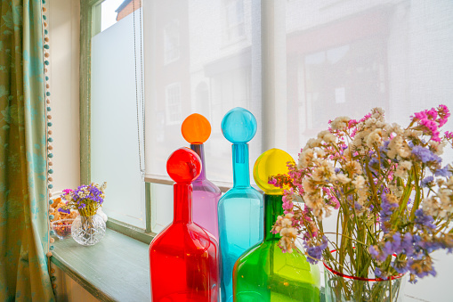 Mixed colorful bottles and flowers on window sill bright red, blue, green and orange.