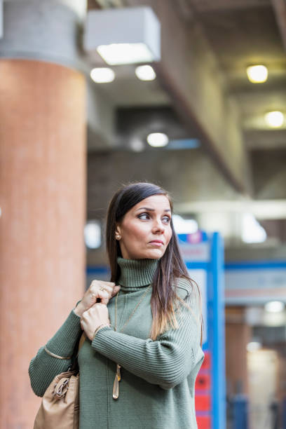 Mature mixed race Hispanic woman in train station A mature mixed race Hispanic and Caucasian woman in her 40s in the city, on her way to work, walking along a train station platform. She is looking away with a serious expression. She is holding onto the strap of her shoulder bag. looking around stock pictures, royalty-free photos & images