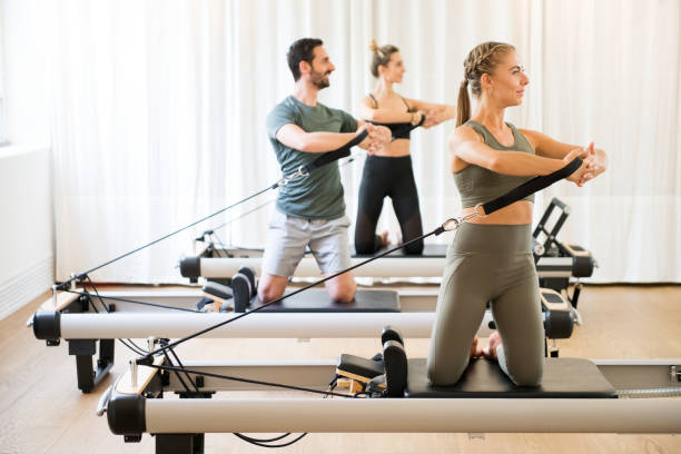Three people exercising torson rotation at gym Three people exercising torson rotation at gym using pilates reformer beds pilates photos stock pictures, royalty-free photos & images