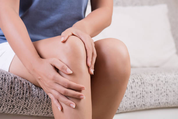 closeup young woman sitting on sofa and feeling knee pain and she massage her knee at home. healthcare and medical concept. - osteoarthritis doctor medicine healthcare and medicine imagens e fotografias de stock