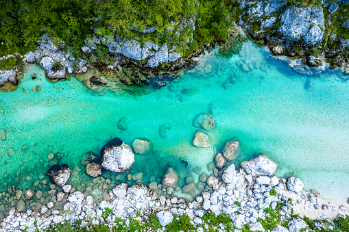 Drone high-angle photo of the turquoise-colored mountain river flowing in the pine woodland with a view of the mountain peaks in the background in Innlandet County, Norway