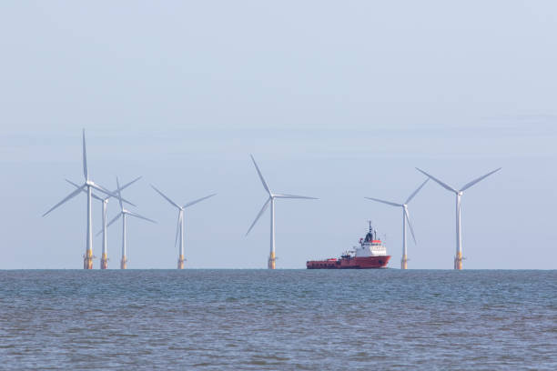 Offshore wind farm turbines with maintenance supply vessel ship Renewable energy offshore wind farm turbines with passing maintenance supply vessel ship. Windfarm on the sea horizon with boat sailing between towers. Sustainable resource green power development. offshore wind farm stock pictures, royalty-free photos & images