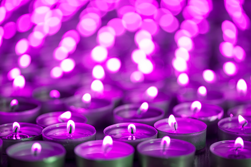Purple pink candle light. Christmas or Diwali celebration tealight candlelight. Lit candles at night vigil. Close-up selective focus image of beautiful night light flames with blurred background.