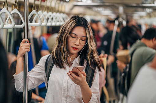 Young woman standing in a bus/subway and using phone