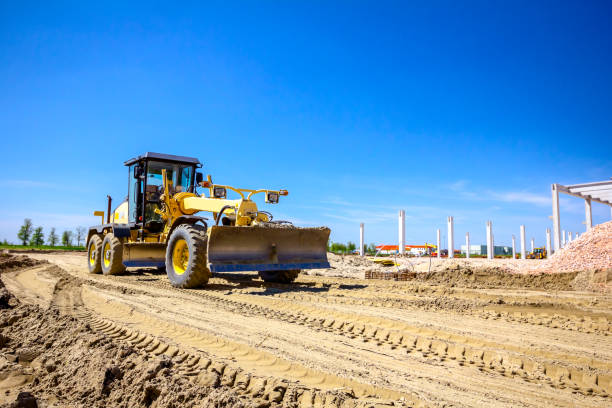 Grader is leveling ground at construction site Operator is driving yellow grader, leveling ground at building site. road scraper stock pictures, royalty-free photos & images