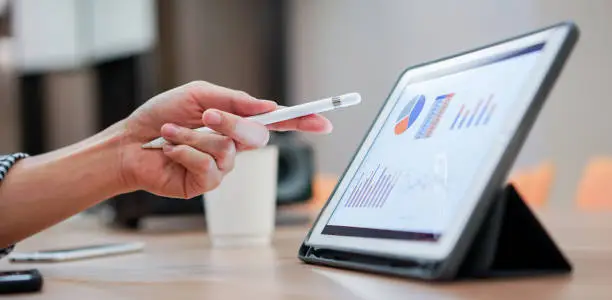 Photo of close up salesman employee hand using stylus pen to pointing on tablet screen to show company profit monthly in the meeting event at conference room , business strategy concept