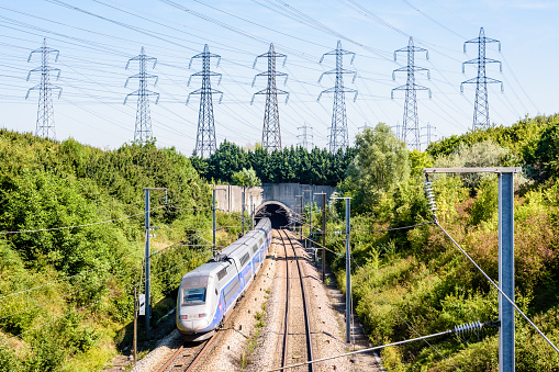 Villebon-sur-Yvette, France - August 25, 2019: A double-decker TGV Duplex high-speed train in Atlantic livery is entering a tunnel under a row of transmission towers on the LGV Atlantique railway.