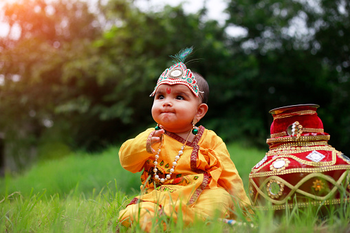 Little baby Krishna sitting with matki outdoors in the nature. Krishna Janmashtami, also known simply as Janmashtami or Gokulashtami, is an annual Hindu festival that celebrates the birth of Krishna, the eighth avatar of Vishnu. Krishna is Devaki and Vasudeva's son and his birthday is celebrated by Hindus as Janmashtami.