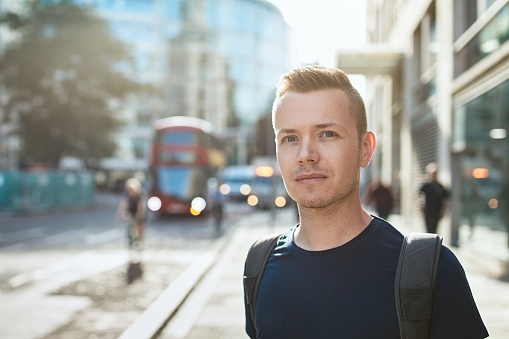 Portrait of young man against city street with bus of public transportation. London, United Kingdom