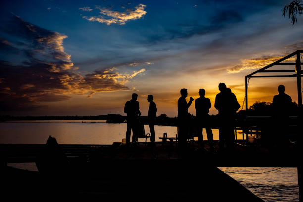 Silhouetted people having a party with drinks on a pier terrace on Niger river outside Niamey against a colorful sunset background during summer Wide angle and telephoto lenses sahel stock pictures, royalty-free photos & images