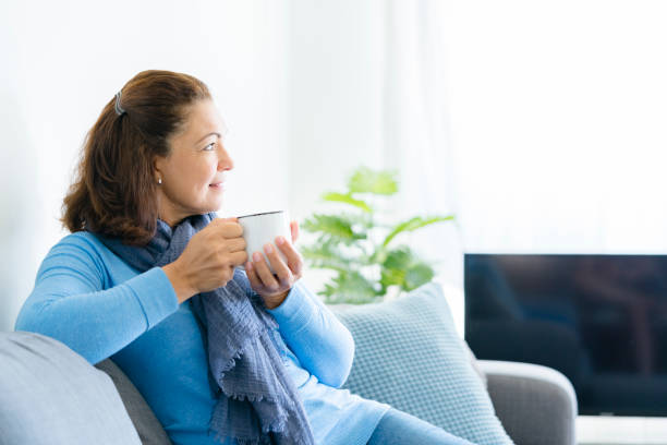 istock Middle aged lady sitting on sofa holding coffee or tea mug 1171291023