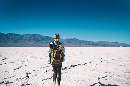 Back view of female traveler exploring death valley national park carrying equipment in rucksack for taking photo,young woman walking on touristic route in beautiful natural landscape on daytime