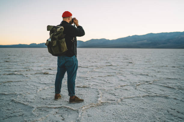 istock Hipster guy traveling in wild environment of lowest point if America using camera for making photos of landscape, back view of skilled photographer taking picture exploring arid lands of Badwater 1171293145