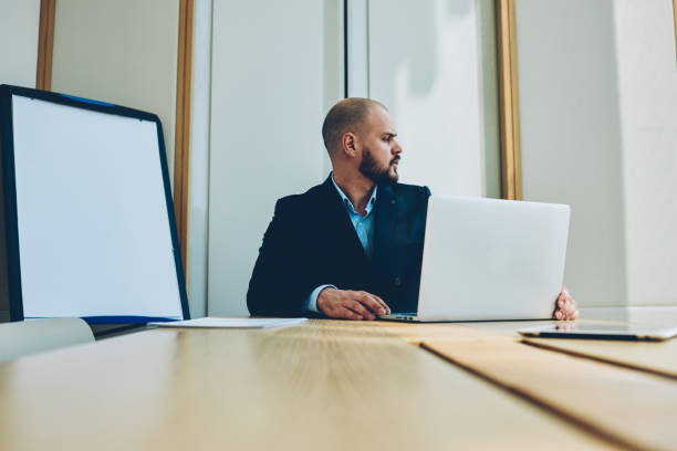 istock Confident male trader looking away while working at modern laptop computer connected to wireless internet.Smart businessman sitting at digital netbook at meeting table in office interior during conference 1171301484