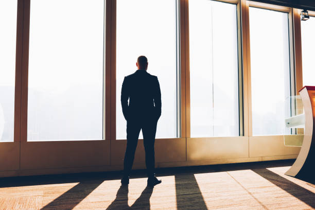 istock Back view of businessman dressed in formal clothes and holding hands in pockets while thinking on creative ideas for developing own company and financial profit while enjoying sunset scenery 1171301501